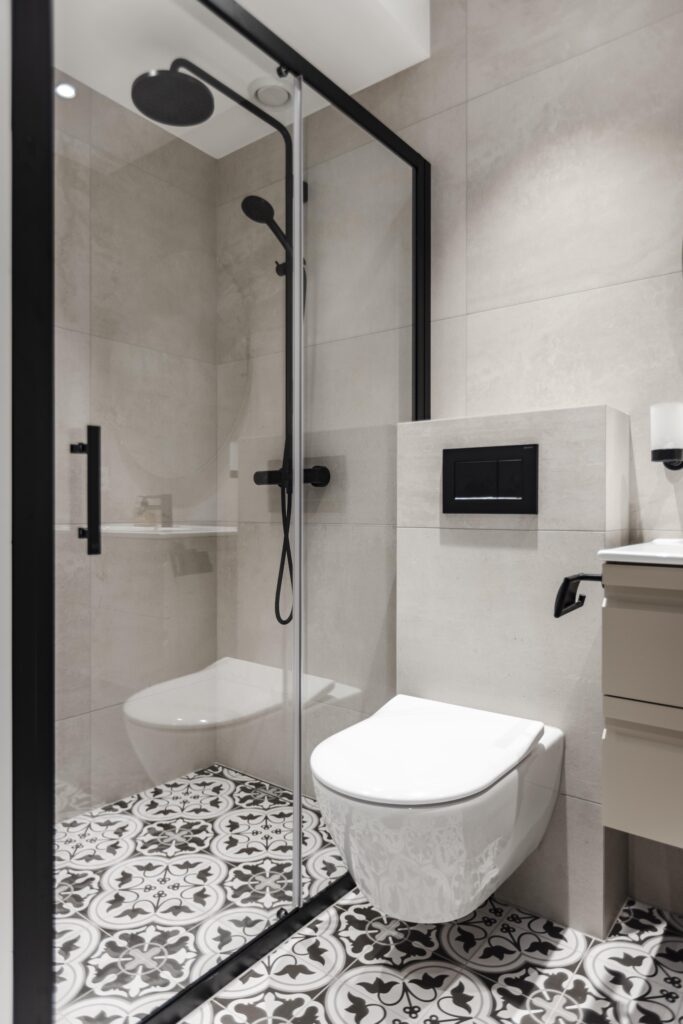 Bad med tradisjonelle fliser på gulv, lyse kvadratiske fliser på vegg, detaljer og armaturer i matt sort og hvitt toalett. Badet er totalrenovert av Lomundal.